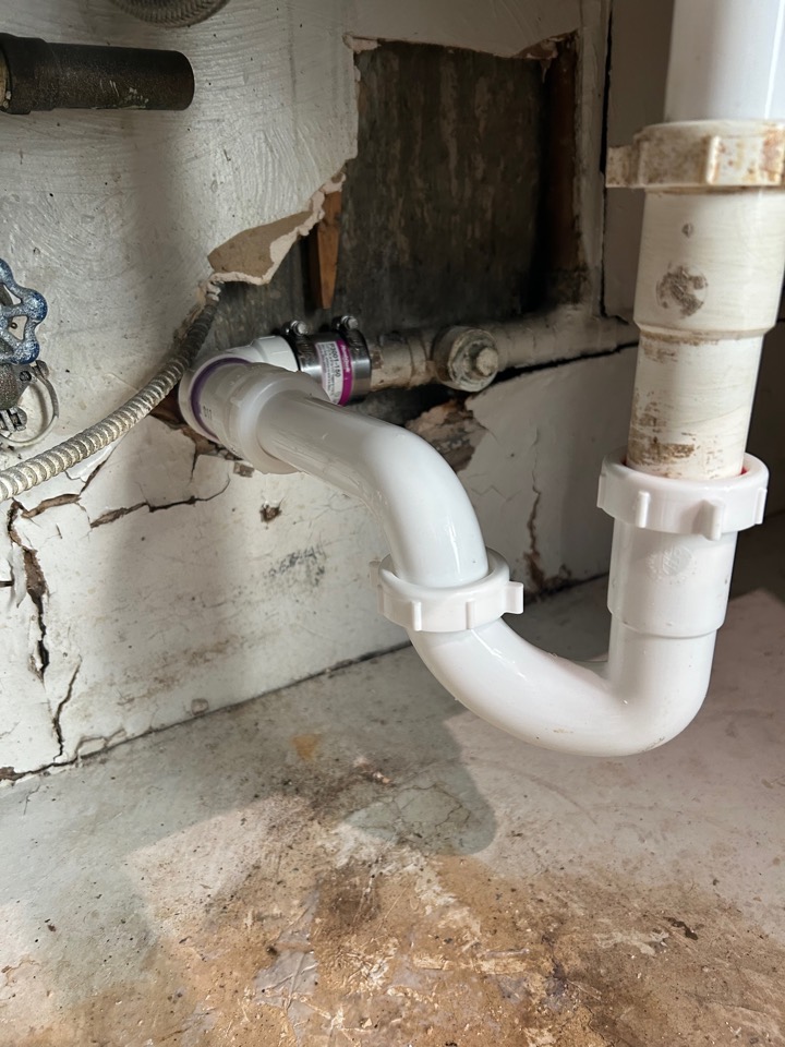 A new white PVC drain installed behind an opened wall under a sink