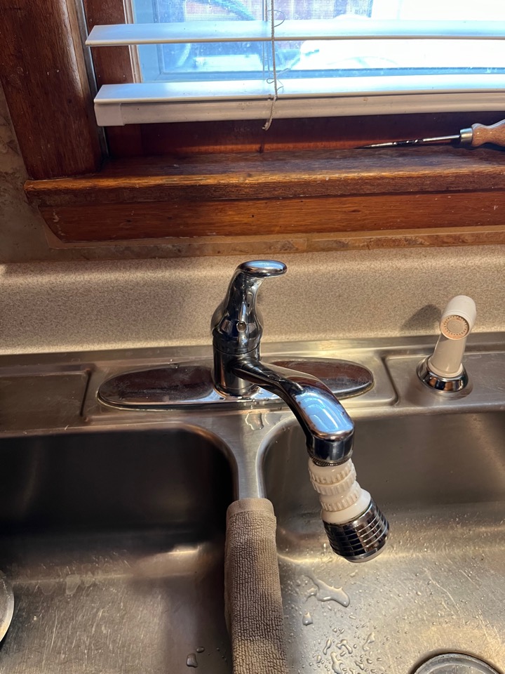 An old single-handle kitchen faucet with a clip-on sprayer at a stainless double sink