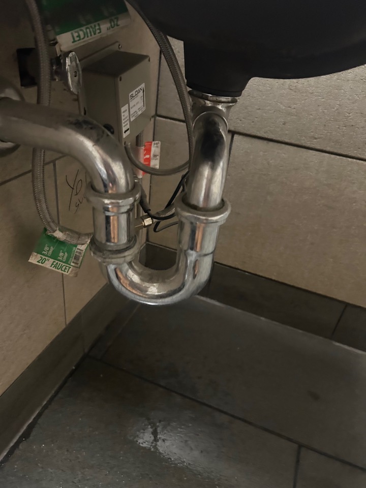A leaking chrome P-trap under a bathroom sink, with water on the floor