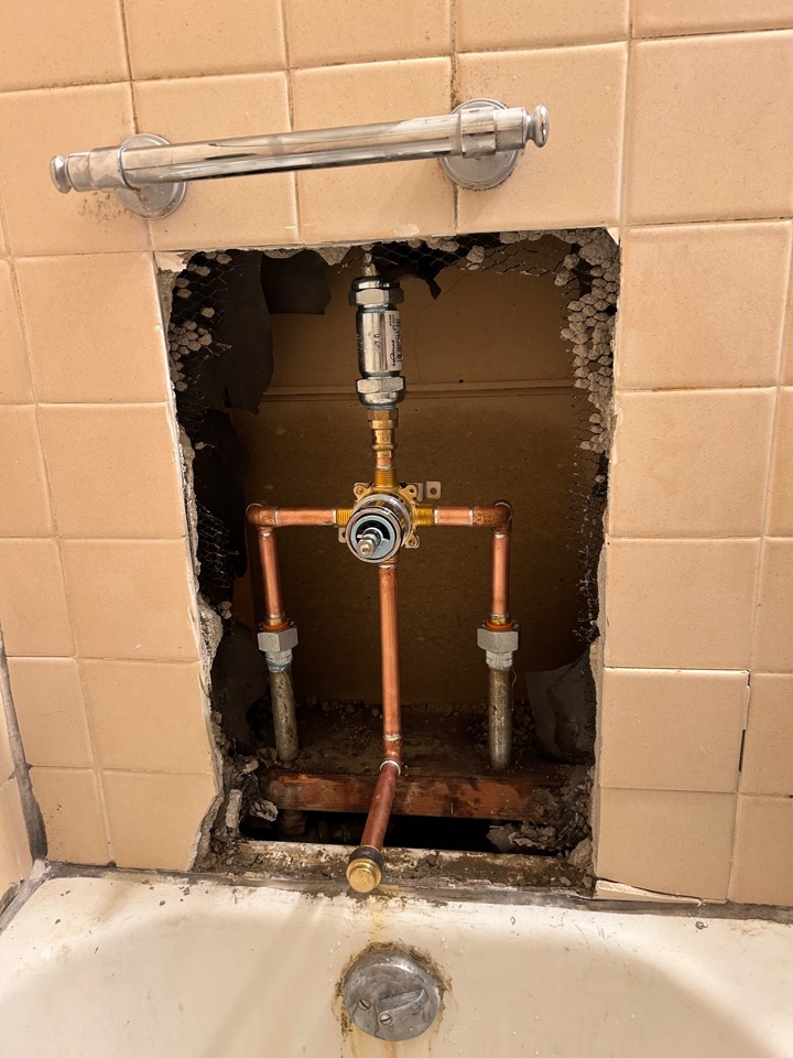 A new single-handle shower valve on copper lines inside the opened wall