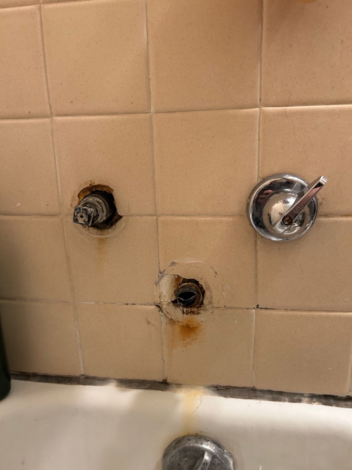 An old three-handle shower valve with corroded openings in the tile
