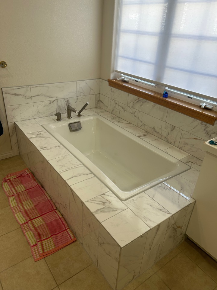 A drop-in soaking tub set in a marble-look tile deck, with a deck-mounted faucet and hand shower