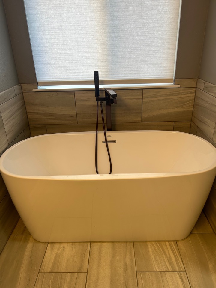 A freestanding soaking tub with a matte black floor-mounted filler and hand shower