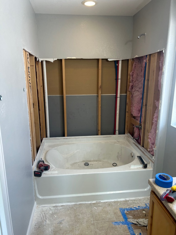 The old surround removed and the wall opened to the studs, with the water lines exposed above the tub